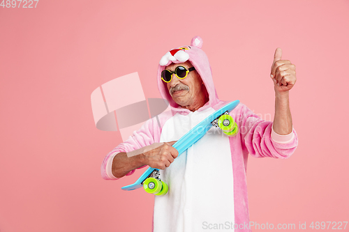 Image of Senior hipster man in stylish pink attire isolated on pink background. Tech and joyful elderly lifestyle concept