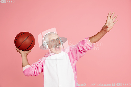 Image of Senior hipster man in stylish pink attire isolated on pink background. Tech and joyful elderly lifestyle concept