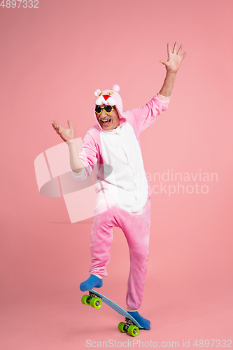 Image of Senior hipster man in stylish pink attire isolated on pink background. Tech and joyful elderly lifestyle concept