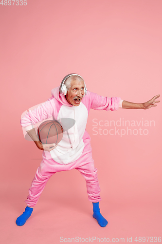 Image of Senior hipster man in stylish pink attire isolated on pink background. Tech and joyful elderly lifestyle concept