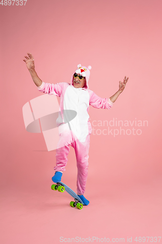 Image of Senior hipster man in stylish pink attire isolated on pink background. Tech and joyful elderly lifestyle concept