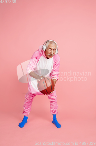 Image of Senior hipster man in stylish pink attire isolated on pink background. Tech and joyful elderly lifestyle concept