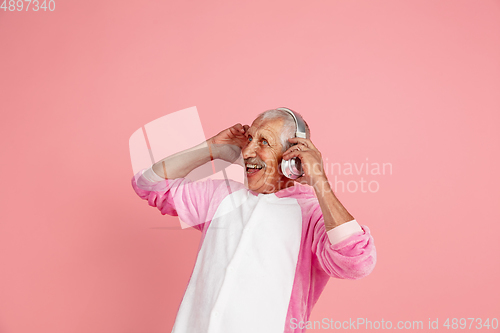 Image of Senior hipster man in stylish pink attire isolated on pink background. Tech and joyful elderly lifestyle concept