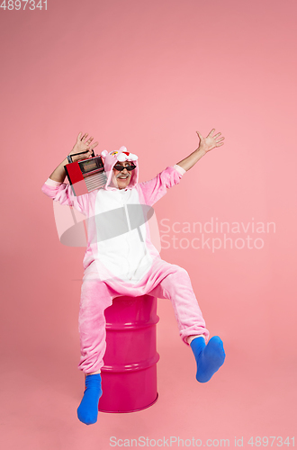 Image of Senior hipster man in stylish pink attire isolated on pink background. Tech and joyful elderly lifestyle concept