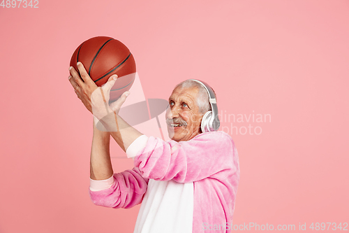 Image of Senior hipster man in stylish pink attire isolated on pink background. Tech and joyful elderly lifestyle concept