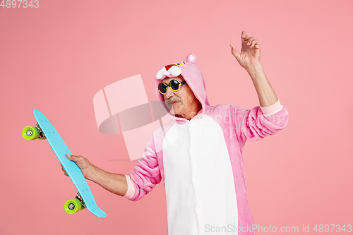 Image of Senior hipster man in stylish pink attire isolated on pink background. Tech and joyful elderly lifestyle concept