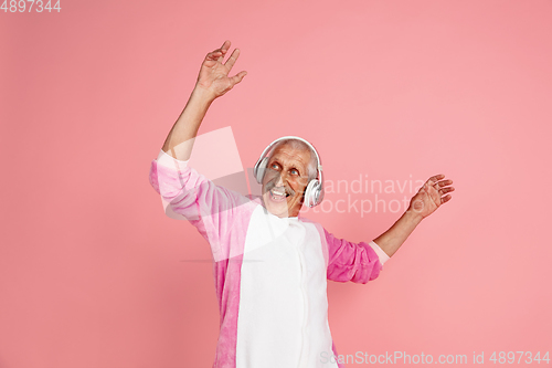 Image of Senior hipster man in stylish pink attire isolated on pink background. Tech and joyful elderly lifestyle concept