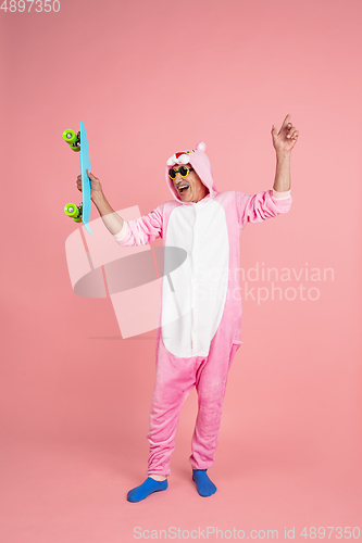 Image of Senior hipster man in stylish pink attire isolated on pink background. Tech and joyful elderly lifestyle concept