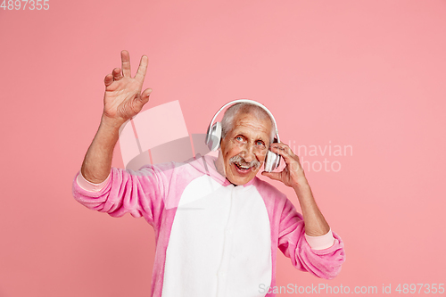 Image of Senior hipster man in stylish pink attire isolated on pink background. Tech and joyful elderly lifestyle concept