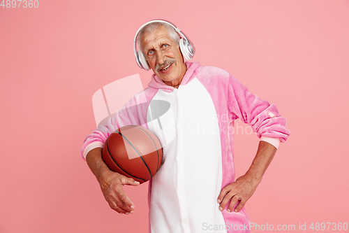 Image of Senior hipster man in stylish pink attire isolated on pink background. Tech and joyful elderly lifestyle concept