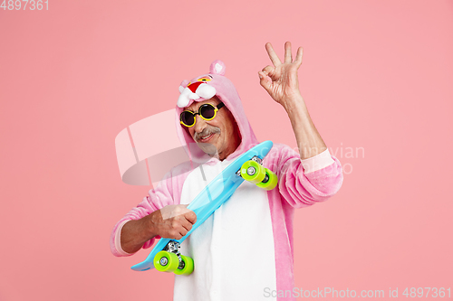 Image of Senior hipster man in stylish pink attire isolated on pink background. Tech and joyful elderly lifestyle concept