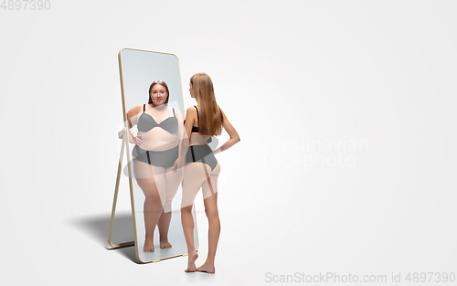 Image of Young slim woman looking at fat girl in mirror\'s reflection on white background