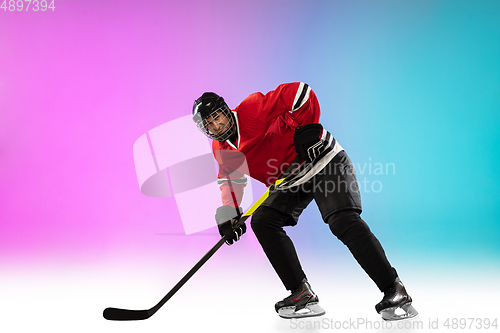 Image of Male hockey player with the stick on ice court and neon colored gradient background. Sportsman wearing equipment, helmet practicing.