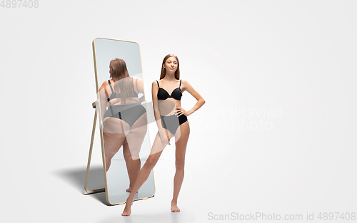 Image of Young slim woman looking at fat girl in mirror\'s reflection on white background