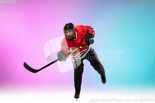 Image of Male hockey player with the stick on ice court and neon colored gradient background. Sportsman wearing equipment, helmet practicing.