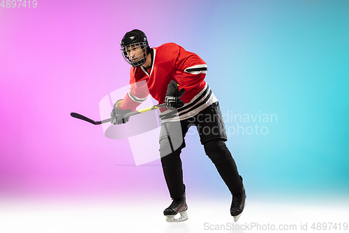 Image of Male hockey player with the stick on ice court and neon colored gradient background. Sportsman wearing equipment, helmet practicing.