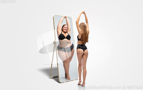 Image of Young slim woman looking at fat girl in mirror\'s reflection on white background