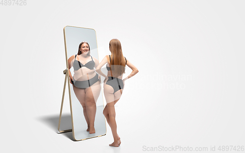 Image of Young slim woman looking at fat girl in mirror\'s reflection on white background