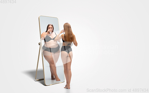 Image of Young slim woman looking at fat girl in mirror\'s reflection on white background