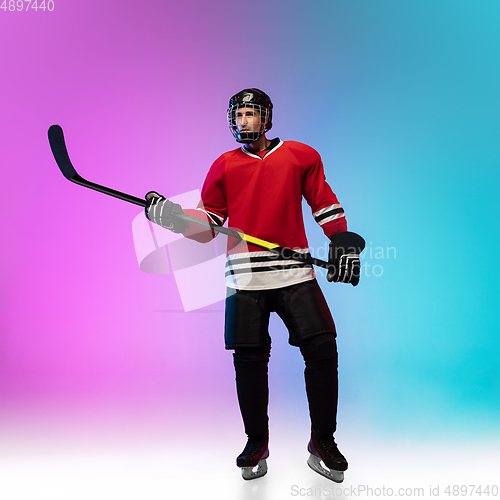 Image of Male hockey player with the stick on ice court and neon colored gradient background. Sportsman wearing equipment, helmet practicing.