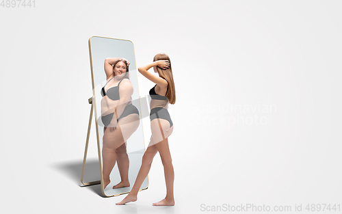 Image of Young slim woman looking at fat girl in mirror\'s reflection on white background