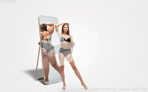 Image of Young slim woman looking at fat girl in mirror\'s reflection on white background