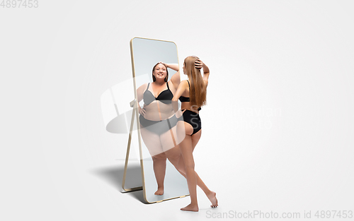 Image of Young slim woman looking at fat girl in mirror\'s reflection on white background