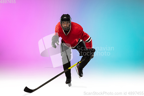 Image of Male hockey player with the stick on ice court and neon colored gradient background. Sportsman wearing equipment, helmet practicing.