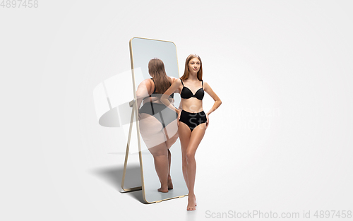 Image of Young slim woman looking at fat girl in mirror\'s reflection on white background