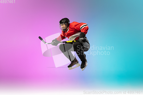 Image of Male hockey player with the stick on ice court and neon colored gradient background. Sportsman wearing equipment, helmet practicing.