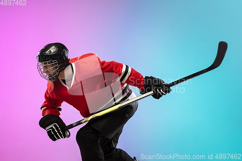 Image of Male hockey player with the stick on ice court and neon colored gradient background. Sportsman wearing equipment, helmet practicing.