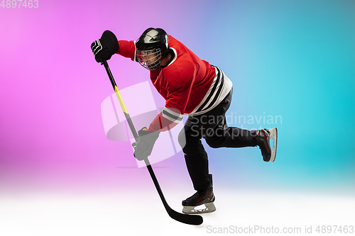 Image of Male hockey player with the stick on ice court and neon colored gradient background. Sportsman wearing equipment, helmet practicing.