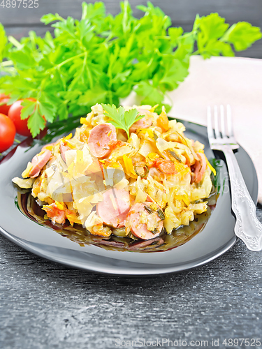 Image of Cabbage stew with sausages in black plate on dark board