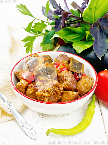 Image of Meat with eggplant and pepper in bowl on wooden board