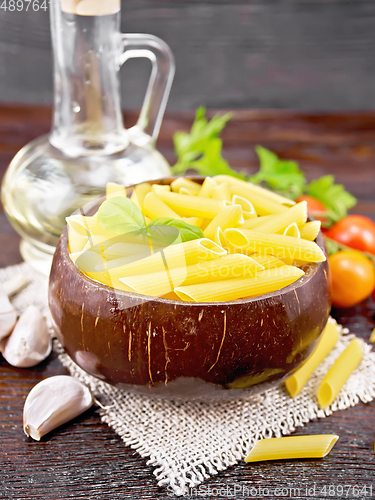 Image of Penne in bowl of coconut with vegetables on brown board