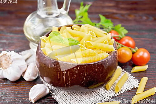 Image of Penne in bowl of coconut with vegetables on wooden board