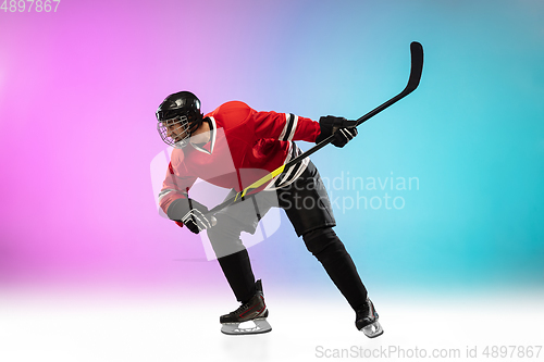 Image of Male hockey player with the stick on ice court and neon colored gradient background. Sportsman wearing equipment, helmet practicing.