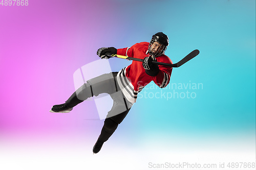 Image of Male hockey player with the stick on ice court and neon colored gradient background. Sportsman wearing equipment, helmet practicing.