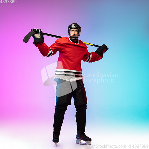 Image of Male hockey player with the stick on ice court and neon colored gradient background. Sportsman wearing equipment, helmet practicing.