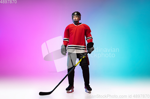 Image of Male hockey player with the stick on ice court and neon colored gradient background. Sportsman wearing equipment, helmet practicing.