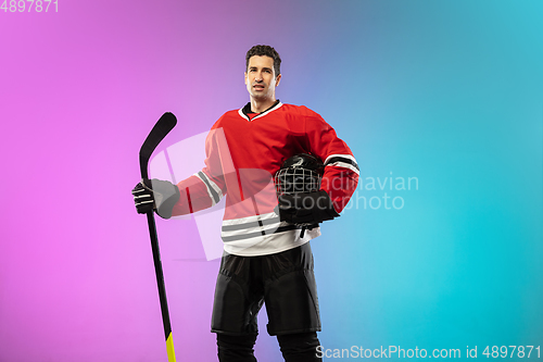 Image of Male hockey player with the stick on ice court and neon colored gradient background. Sportsman wearing equipment, helmet practicing.