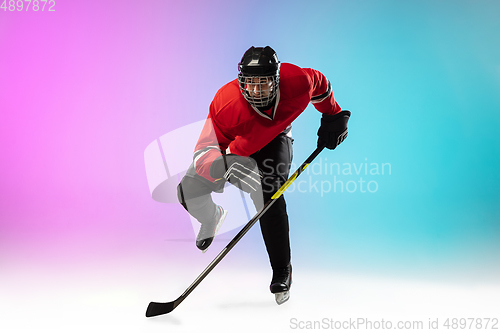 Image of Male hockey player with the stick on ice court and neon colored gradient background. Sportsman wearing equipment, helmet practicing.