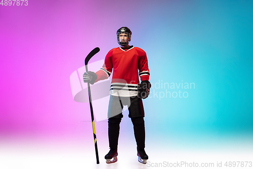 Image of Male hockey player with the stick on ice court and neon colored gradient background. Sportsman wearing equipment, helmet practicing.