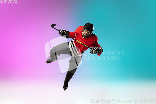 Image of Male hockey player with the stick on ice court and neon colored gradient background. Sportsman wearing equipment, helmet practicing.