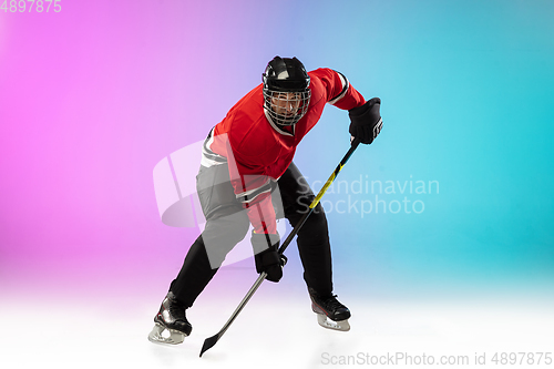 Image of Male hockey player with the stick on ice court and neon colored gradient background. Sportsman wearing equipment, helmet practicing.