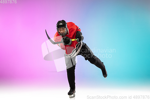 Image of Male hockey player with the stick on ice court and neon colored gradient background. Sportsman wearing equipment, helmet practicing.