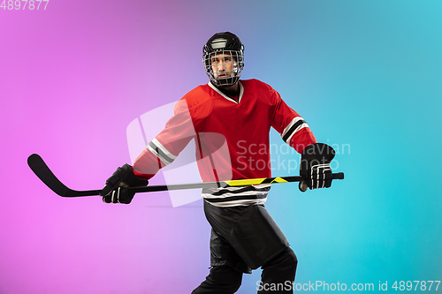 Image of Male hockey player with the stick on ice court and neon colored gradient background. Sportsman wearing equipment, helmet practicing.