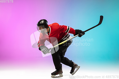 Image of Male hockey player with the stick on ice court and neon colored gradient background. Sportsman wearing equipment, helmet practicing.