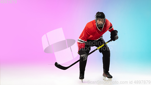 Image of Male hockey player with the stick on ice court and neon colored gradient background. Sportsman wearing equipment, helmet practicing.