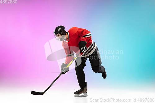 Image of Male hockey player with the stick on ice court and neon colored gradient background. Sportsman wearing equipment, helmet practicing.